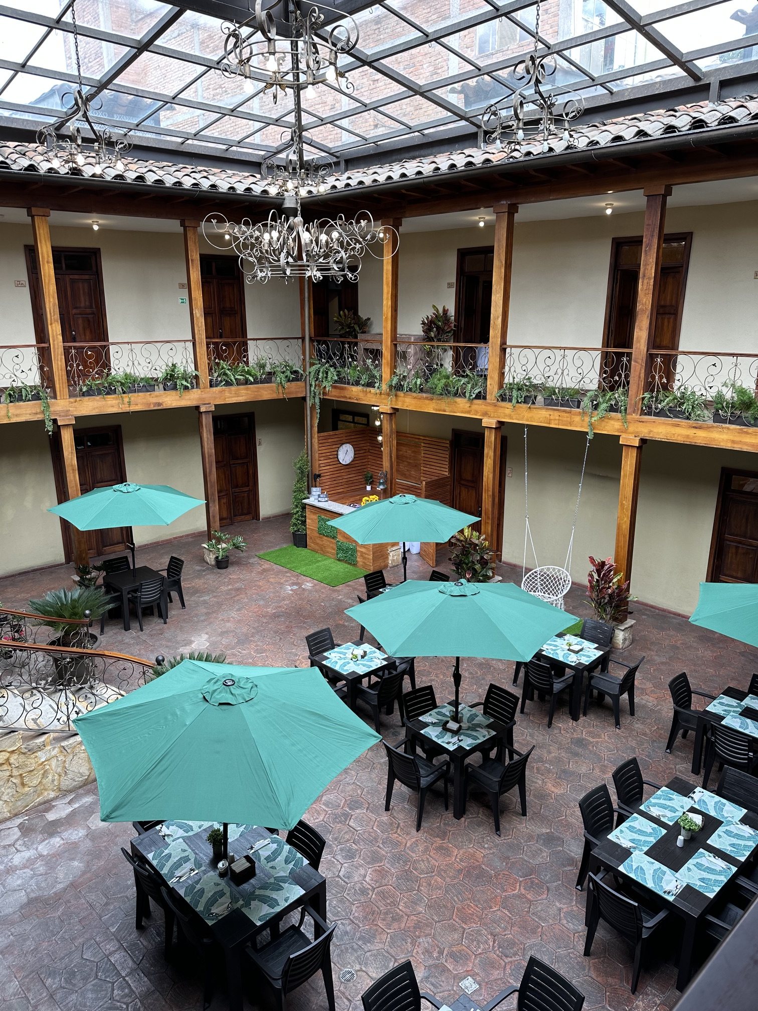 Wooden colonial galleries of Hotel NASS Central Garden under a glass roof with overhead light, Cuenca