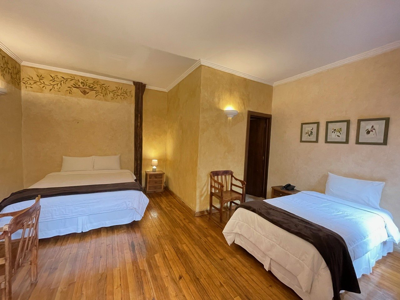 Twin bedroom at Hotel NASS Casa del Águila with terracotta painted walls and wooden floor, restored colonial atmosphere