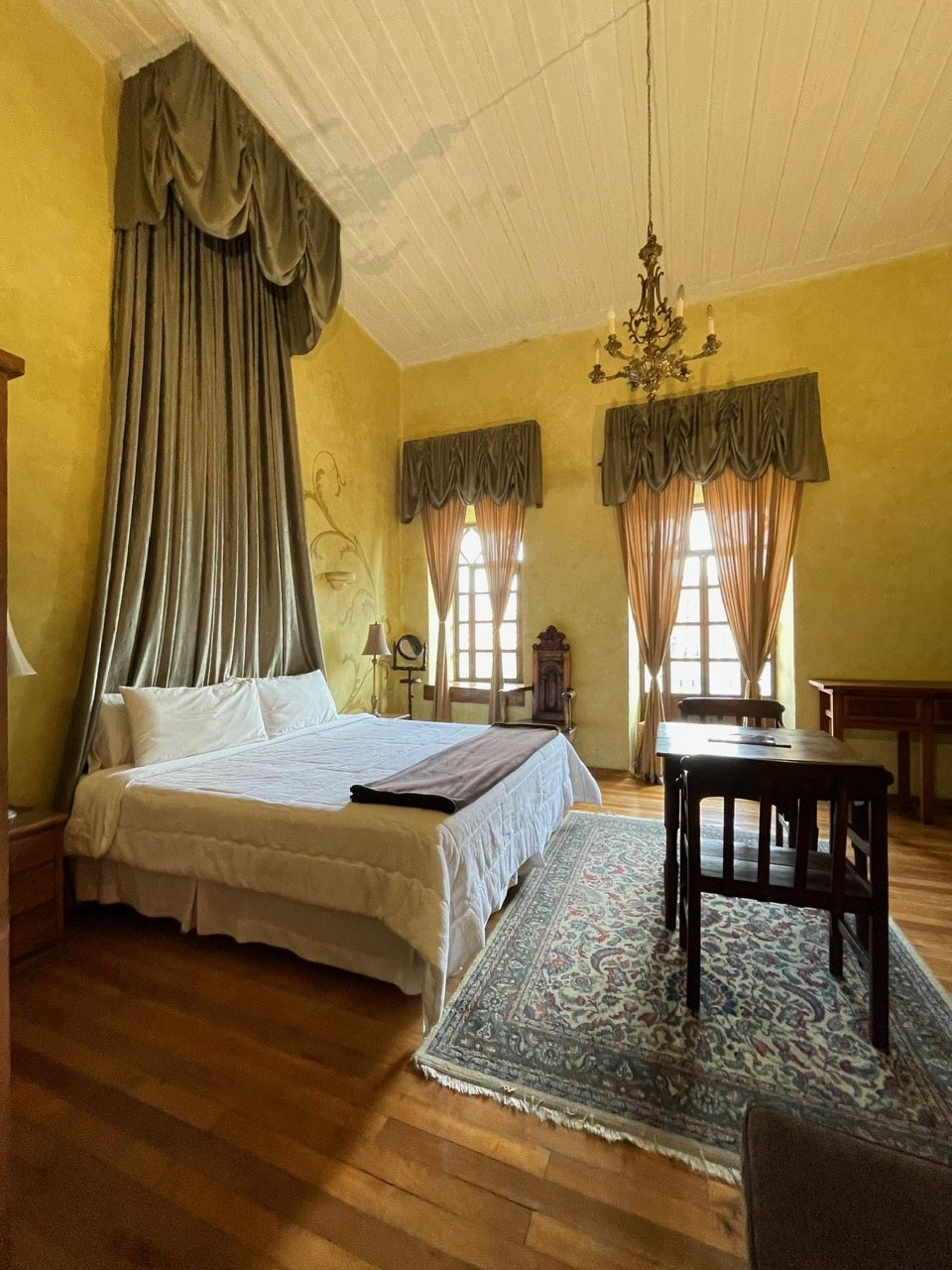 Romantic suite at Hotel NASS Casa del Águila with silk curtains, lounge chair and window over Mariscal Sucre Street, Cuenca