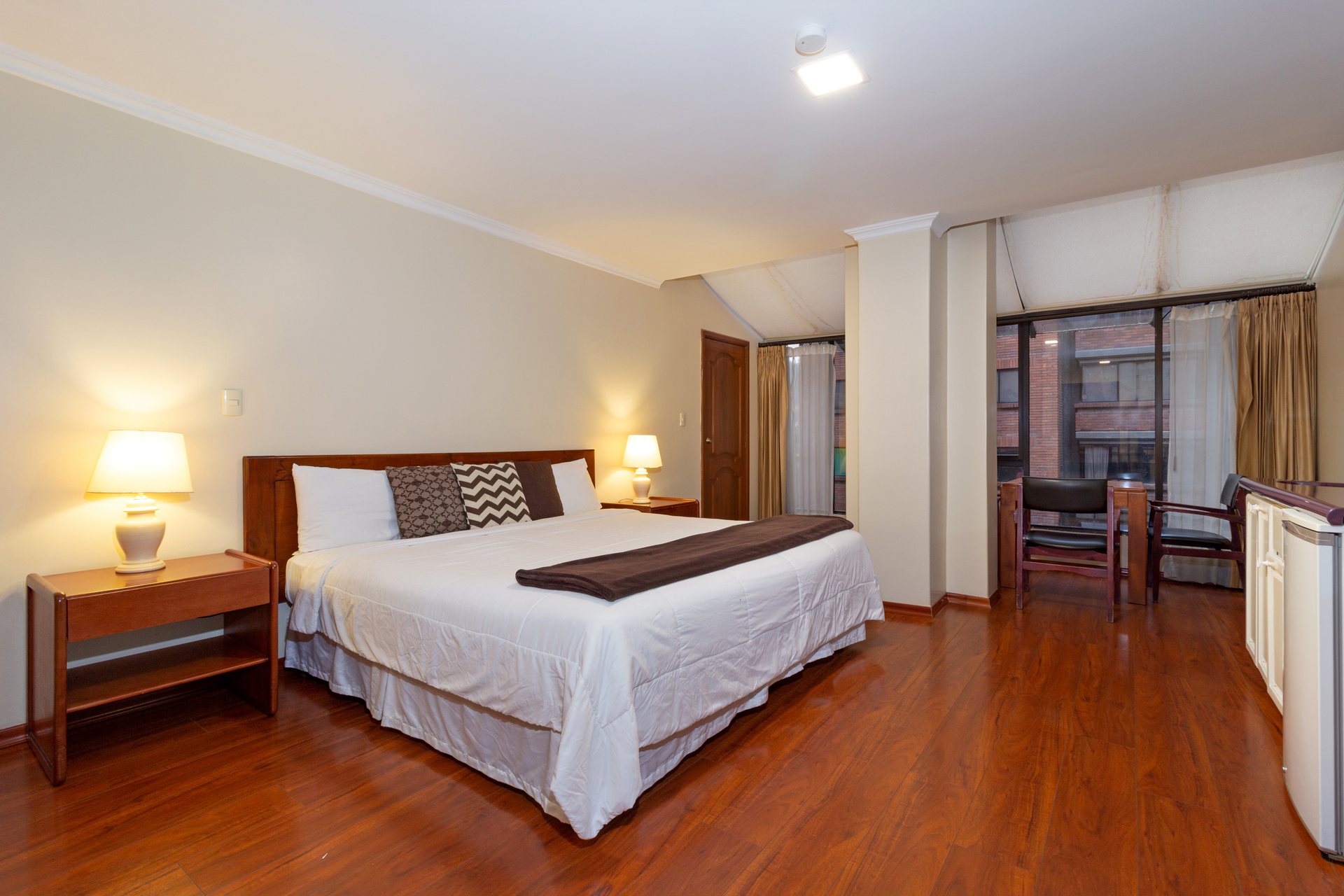 King-size suite at Hotel NASS Pinar del Lago with large windows and a lounge area, next to the Tomebamba River