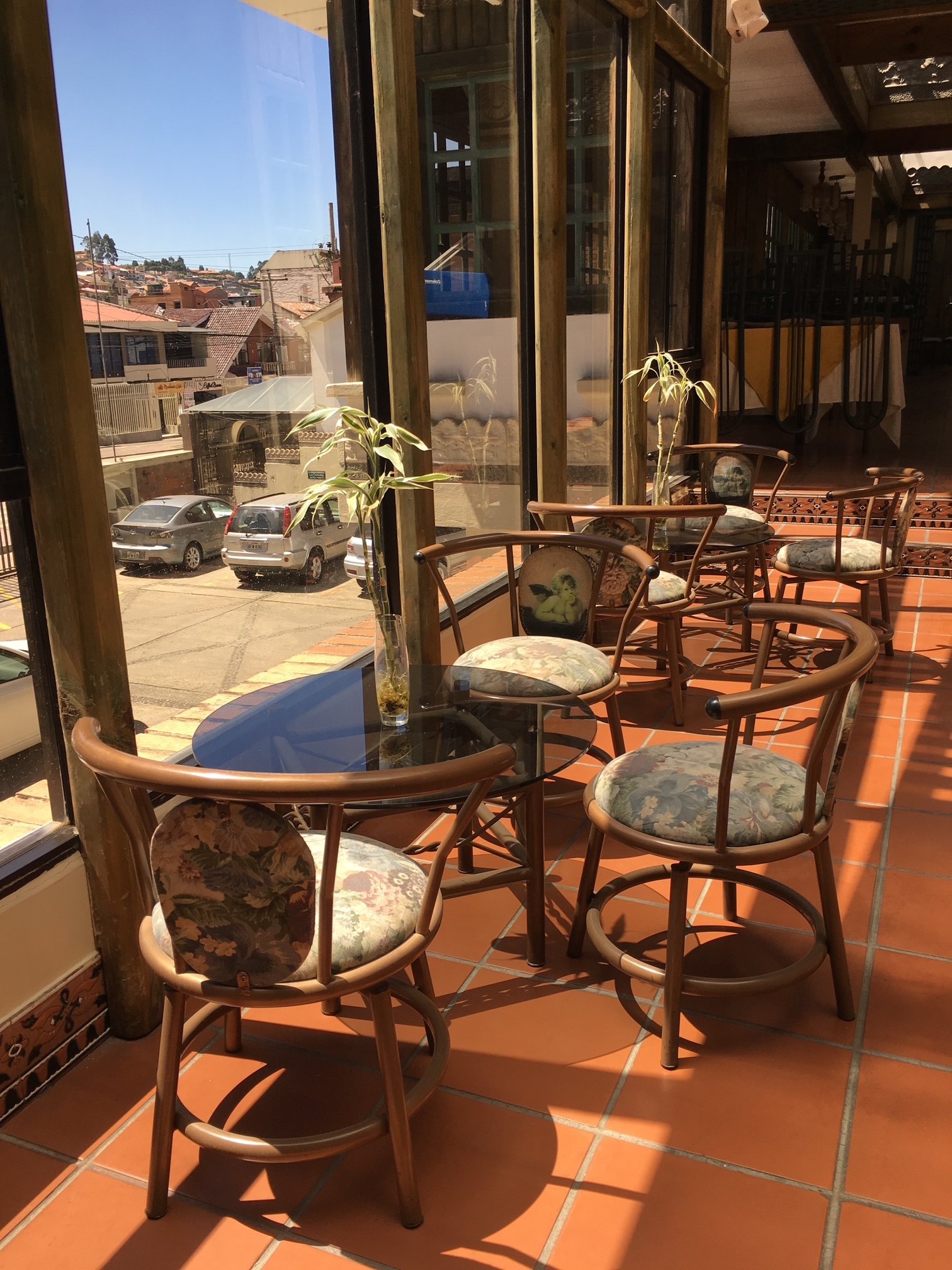 Glass-enclosed terrace at Hotel NASS Pinar del Lago with rattan chairs and a view of the Puertas del Sol residential neighborhood, Cuenca